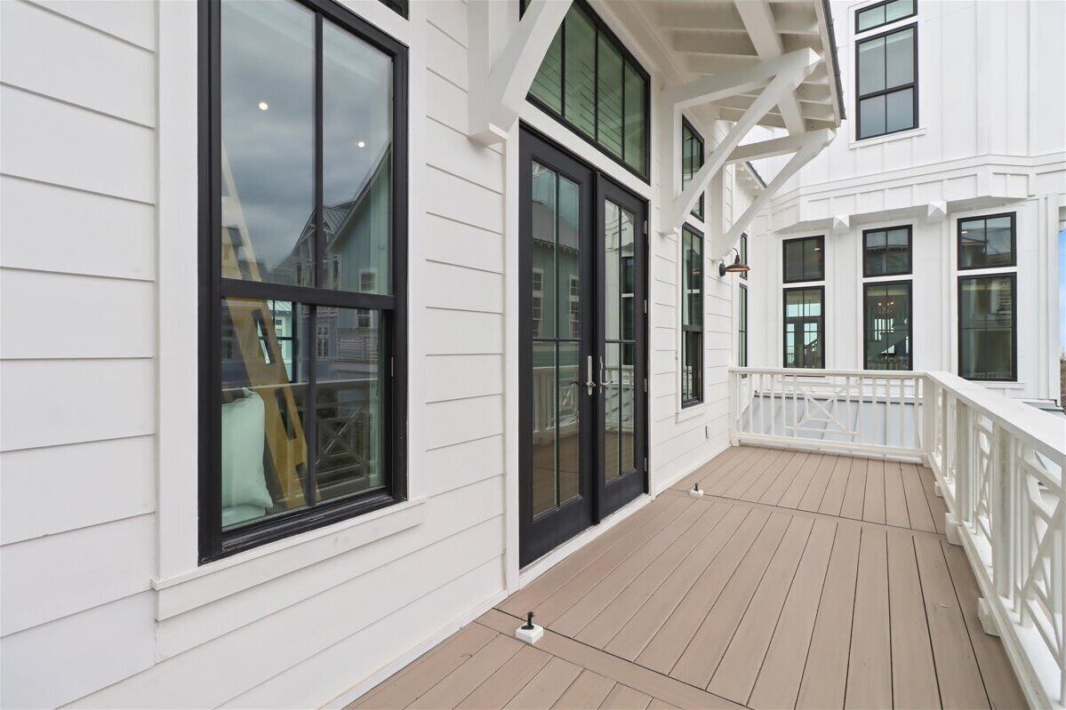 A covered outdoor area with a wooden deck, white walls, and large windows.