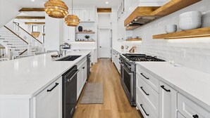 A modern kitchen with white cabinetry, a central island, and a wooden ceiling. - Driftwood Waves 116 LES (Port Aransas)