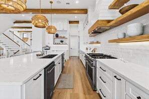 A modern kitchen with white cabinetry, a central island, and a wooden ceiling. - Driftwood Waves 116 LES (Port Aransas)