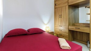 A bedroom with a bed, a wooden wardrobe, a nightstand, and a lamp.