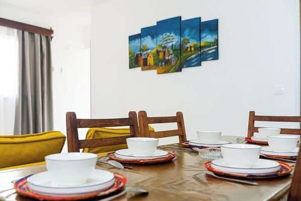 A dining table set with white plates, bowls, and cutlery, surrounded by wooden chairs.