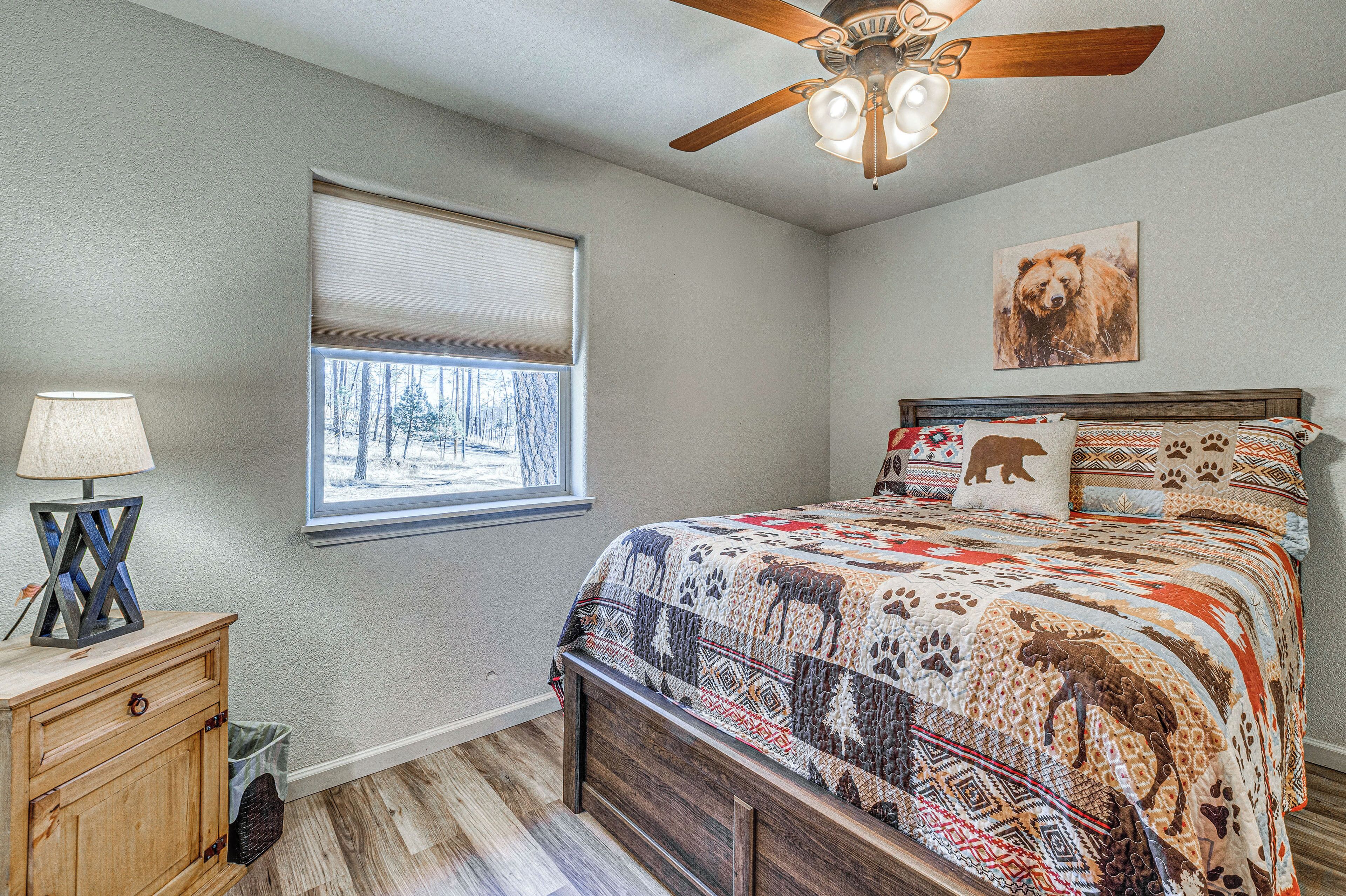 A bedroom with a wooden bed, a ceiling fan, a window with blinds, and a wall-mounted lamp.