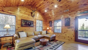 Interior acogedor de una cabaña con un sofá modular, una mesita redonda y una cabeza de venado montada.