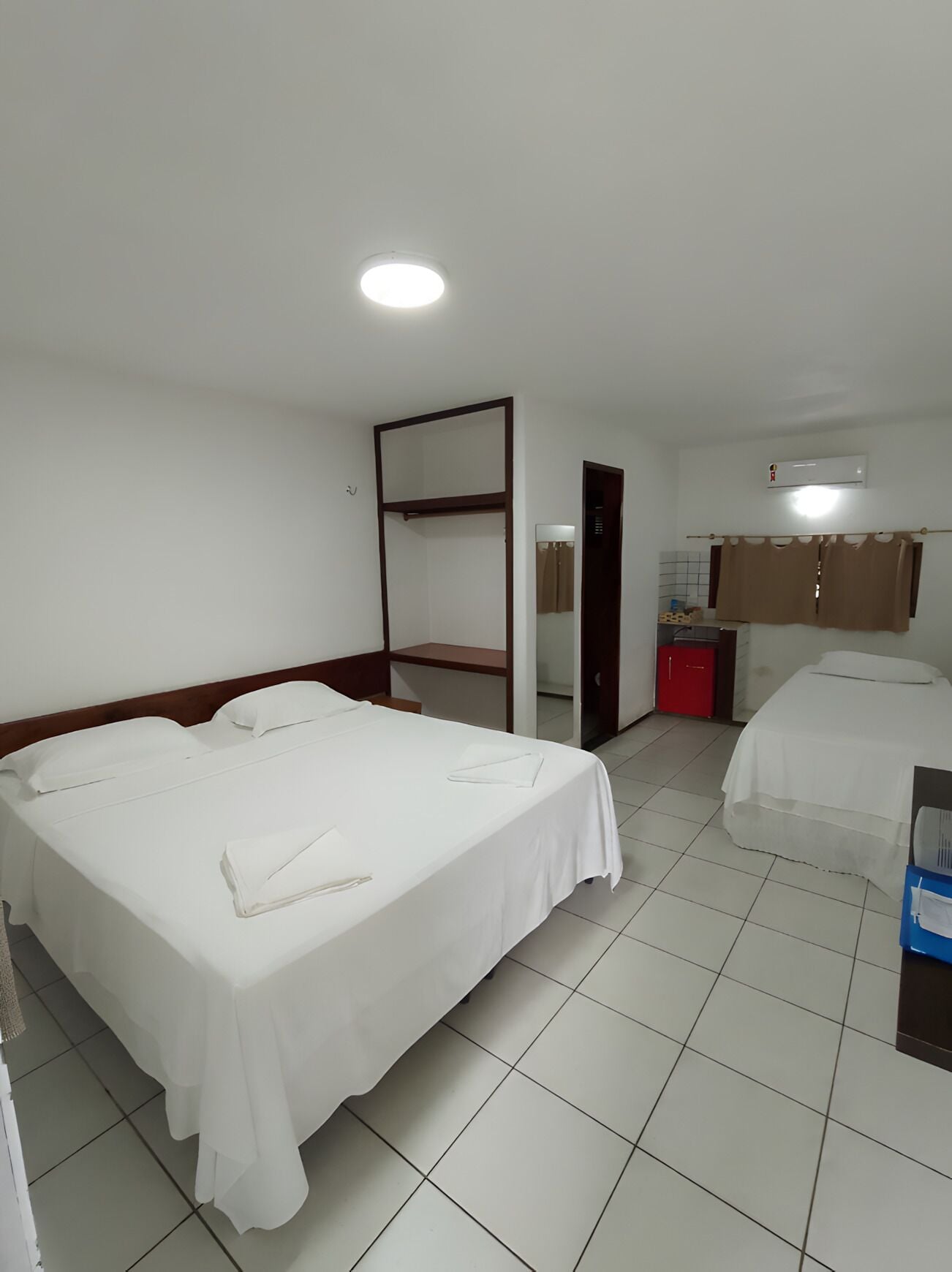 Hotellihuone, jossa on kaksi sänkyä, vaatekaappi, peili, pieni keittokomero ja ilmastointilaite.