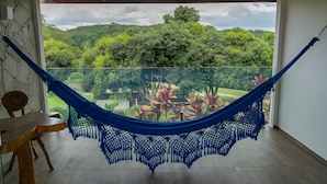 Un hamac dans une pièce donnant sur un jardin luxuriant et des collines.