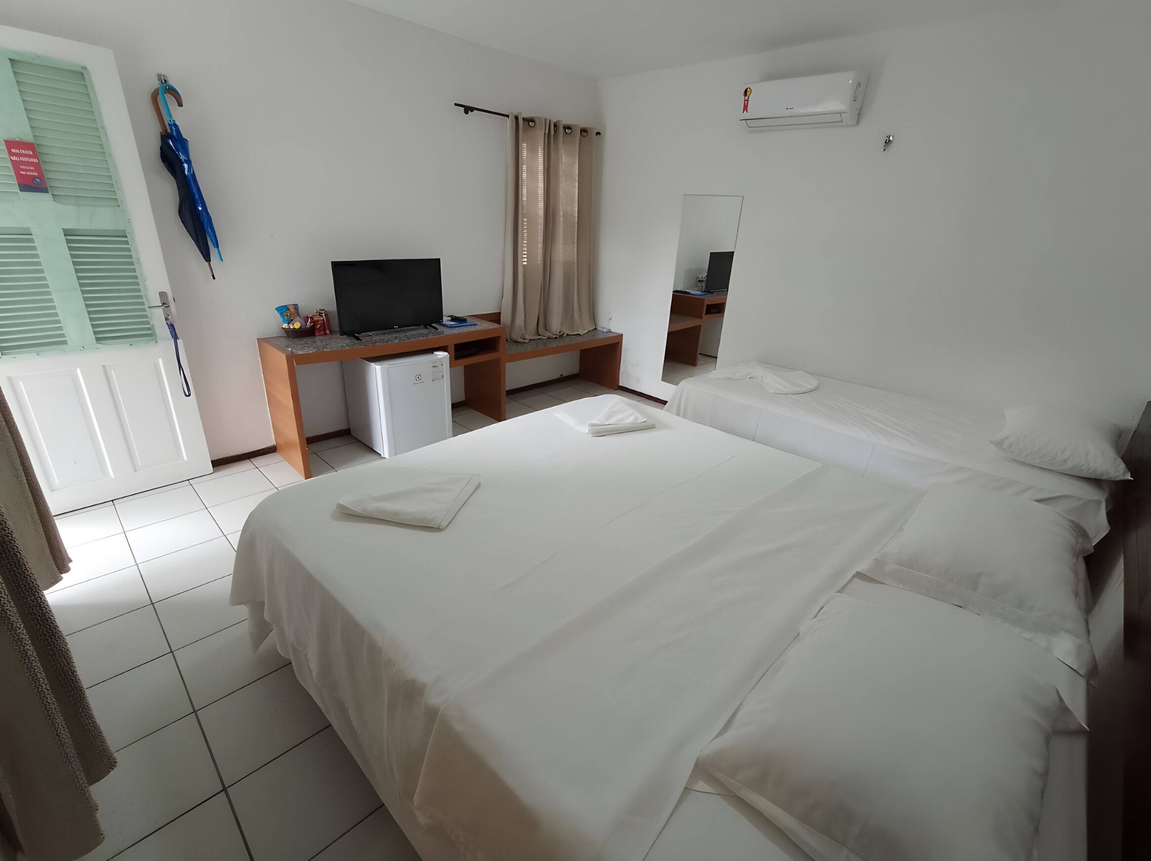 A hotel room with a bed, a desk with a computer, a television, and a mirror.