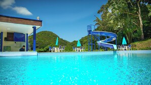 Une piscine avec un toboggan, des chaises longues et un bâtiment doté d’un toit bleu.