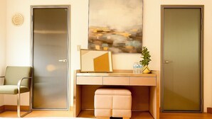 Ein modernes Hotelzimmer mit einem Bett, einem Schreibtisch mit Stuhl, einem großen abstrakten Gemälde und zwei Türen.