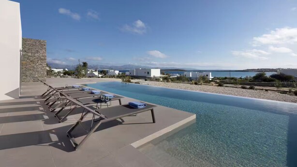 A pool area with lounge chairs and a stone wall, overlooking a body of water and distant mountains. - Celestial Villa I (Santa Maria)