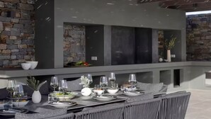 An outdoor dining area with a stone wall backdrop, a modern bar counter, and a seating arrangement. - Celestial Villa I (Santa Maria)