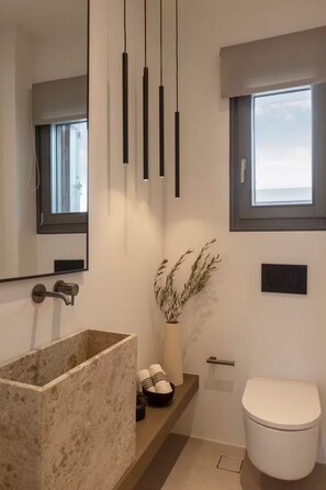 A modern bathroom with a large stone sink, a toilet, a window, and a mirror. - Celestial Villa I (Santa Maria)
