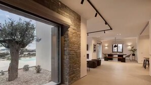 A modern interior with a stone wall, a large window, and a dining area with a pool view. - Celestial Villa I (Santa Maria)