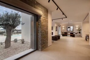 A modern interior with a stone wall, a large window, and a dining area with a pool view. - Celestial Villa I (Santa Maria)