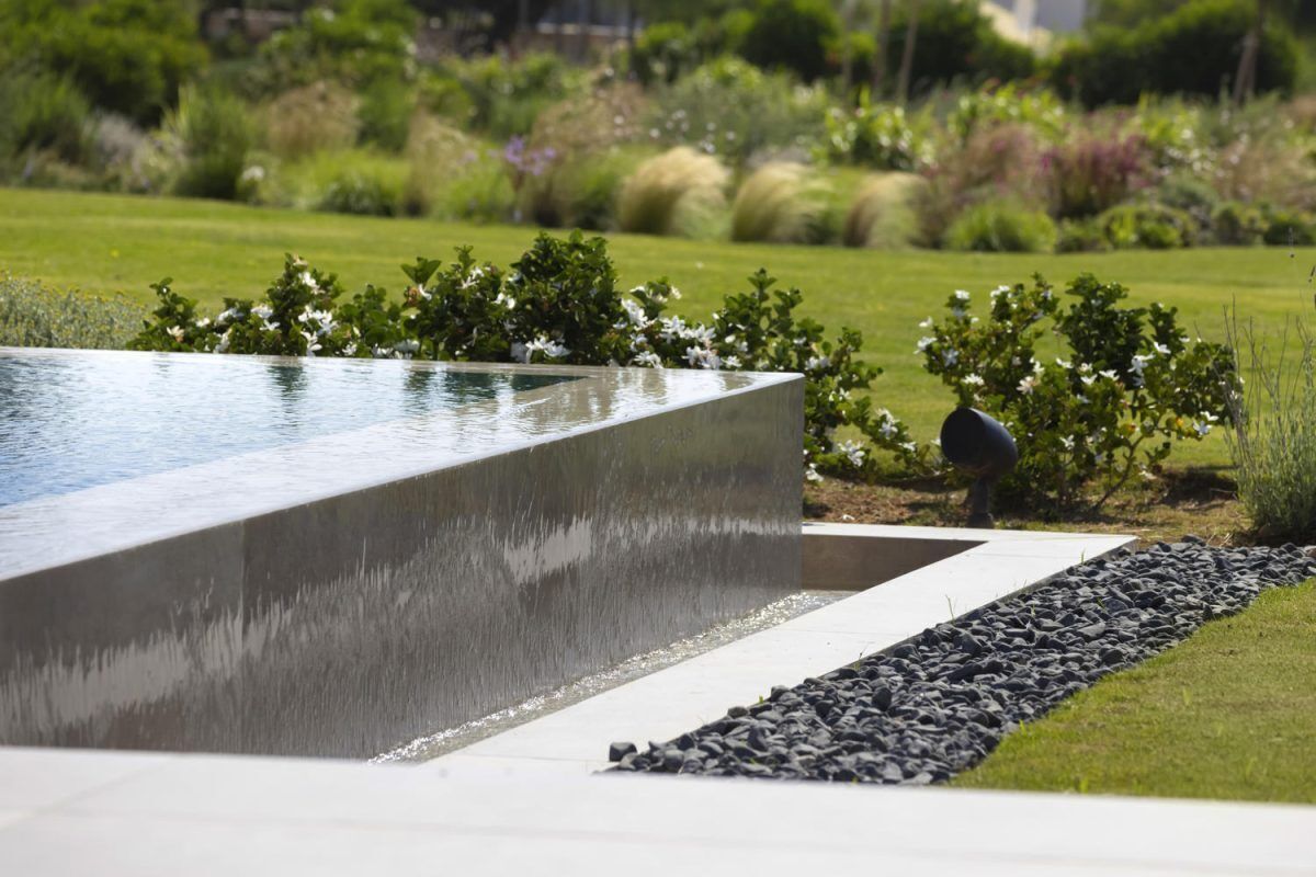 Un área de piscina exterior moderna con borde de hormigón, rodeada de césped y arbustos bien cuidados.