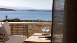 Ein Balkon mit Meerblick, ein Korbstuhl und zwei Gläser auf einem Tisch.