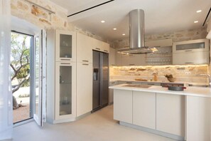 A modern kitchen with white cabinetry, a stainless steel range hood, and a large island with a sink. - Villa Caelia (Santa Maria)