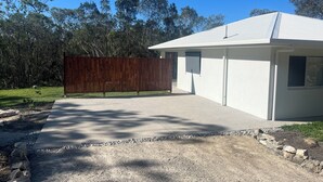 A modern building with a concrete driveway, a wooden fence, and a gravel path. - Private 2-bedroom cottage in tranquil Koah (Koah)