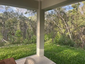 A covered outdoor area with a view of a grassy field and dense trees.