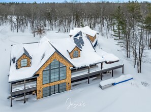 En hytte med stor garage og en overdækket veranda, omgivet af et sneklædt landskab.