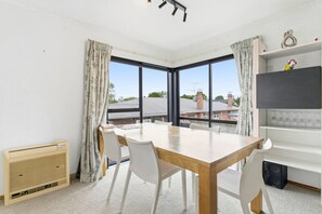 Une chambre moderne dotée d’une grande fenêtre, d’une table à manger avec des chaises, d’un radiateur et d’une étagère ornée d’objets décoratifs.