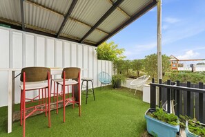 Een overdekt terras met kunstgras, twee rode stoelen, een witte stoel en een blauwe stoel.