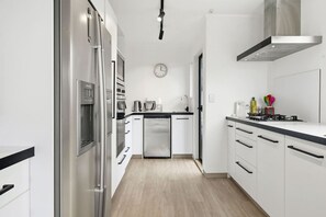 Une cuisine moderne dotée d’appareils électroménagers en acier inoxydable, de meubles blancs et d’un plancher en bois.
