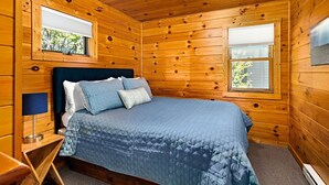 A wooden cabin room with a bed, two windows, and a view of greenery outside. - Charming cabin only feet from Lake Superior (Two Harbors)