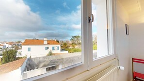 A room with a view of a residential area, a window with a white frame, and a radiator on the wall. - Le Tassigny (Saint-Gilles-Croix-de-Vie)