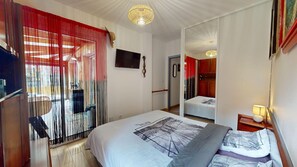 Une chambre à coucher avec un lit, une télévision, un miroir et une porte donnant sur une autre pièce.