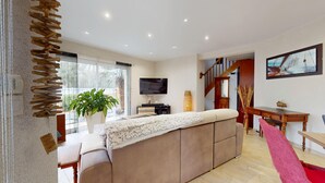 A living room with a sofa, TV, potted plant, and a staircase. - La Villa du Rocher Vert (Saint-Brevin-les-Pins)