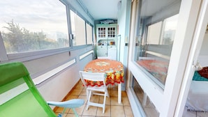 A balcony with a table and chairs, a small cabinet, and a view of buildings. - Nautica - 1-Bedroom Apartment Near the Beach & Parking (Saint-Hilaire-de-Riez)