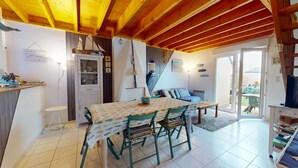 A cozy room with a wooden ceiling, a dining table with chairs, a small kitchen area, and a sliding glass door leading to an outdoor area. - Escapade Turballaise - House 400m from the Port (La Turballe)