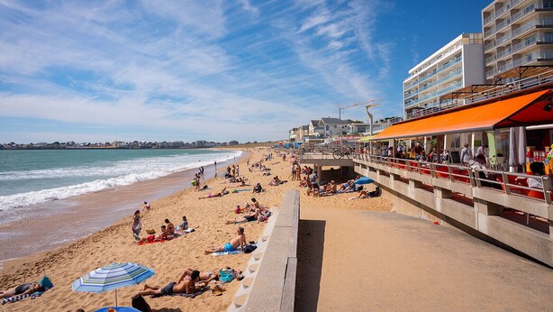 Una playa con un paseo marítimo, sombrillas y un edificio con toldo rojo.