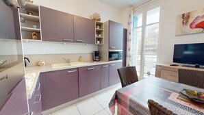 Cocina moderna con horno empotrado, microondas y cafetera. Cuenta con comedor con mesa y sillas, y un televisor sobre un mueble.