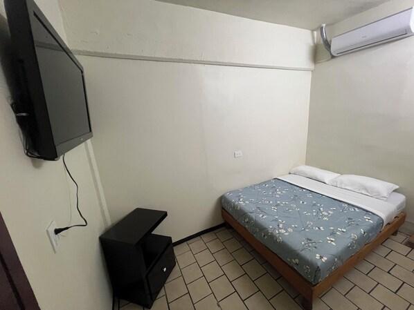 A small bedroom with a bed, a TV mounted on the wall, and a heater. - Hotel Kataluma (Delicias)