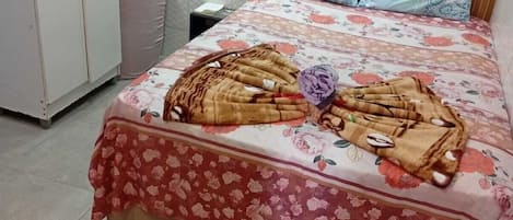 A bedroom with a bed, floral bedspread, pillows, and a wooden headboard.