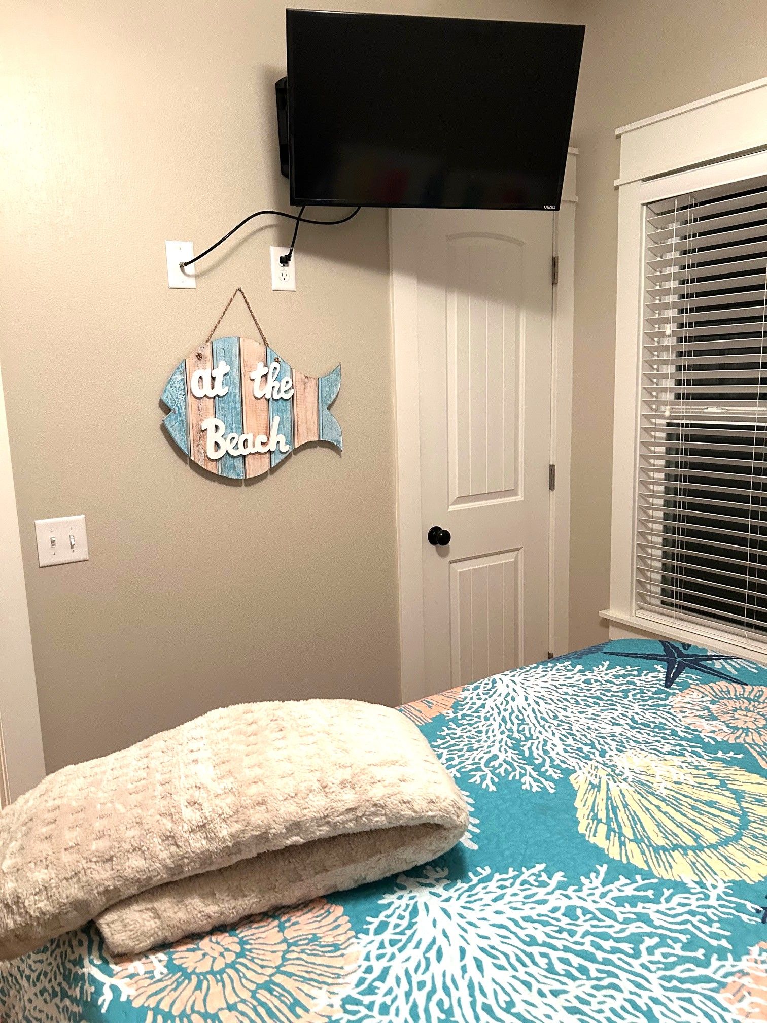 Une chambre à coucher avec un lit, un téléviseur fixé au mur, une porte et un élément de décoration murale.