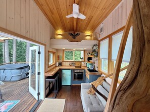 L’intérieur d’une cabane comprend une cuisine, un coin repas et une grande fenêtre donnant sur une forêt.