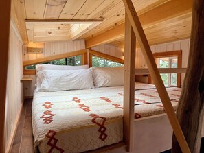 Une chambre de style cabane avec un lit superposé, des poutres en bois au plafond et une fenêtre donnant sur l’extérieur.