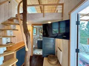 Un intérieur en bois avec un escalier, un téléviseur et une porte donnant sur une cuisine.