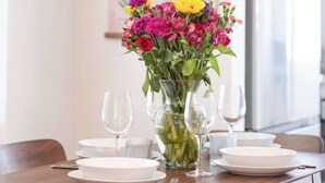 Ein Esstisch ist gedeckt mit weißen Tellern, Gläsern und einer Vase mit Blumen.