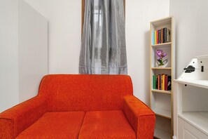 A room with a red armchair, a bookshelf with books and a flower, and a window with a curtain. - Venice Mestre Private Home - (Easy Access to Venice) (Venezia)