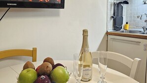 Een keuken met een televisie waarop een open haard te zien is, een champagnefles, twee glazen en een schaal met fruit op tafel.