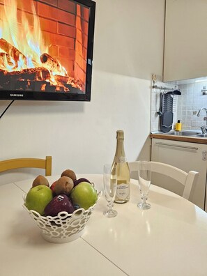 A kitchen with a TV displaying a fireplace, a bottle of champagne, two glasses, and a fruit bowl on the table. - Venice Mestre Private Home - (Easy Access to Venice) (Venezia)