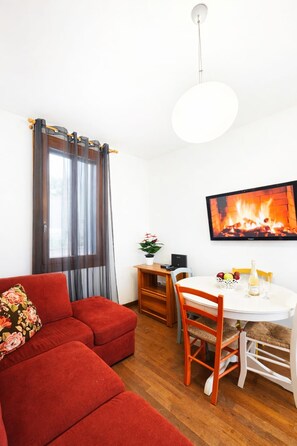 A cozy living room with a red sofa, a dining table with chairs, a flat-screen TV mounted on the wall, and a fireplace. - Venice Mestre Private Home - (Easy Access to Venice) (Venezia)