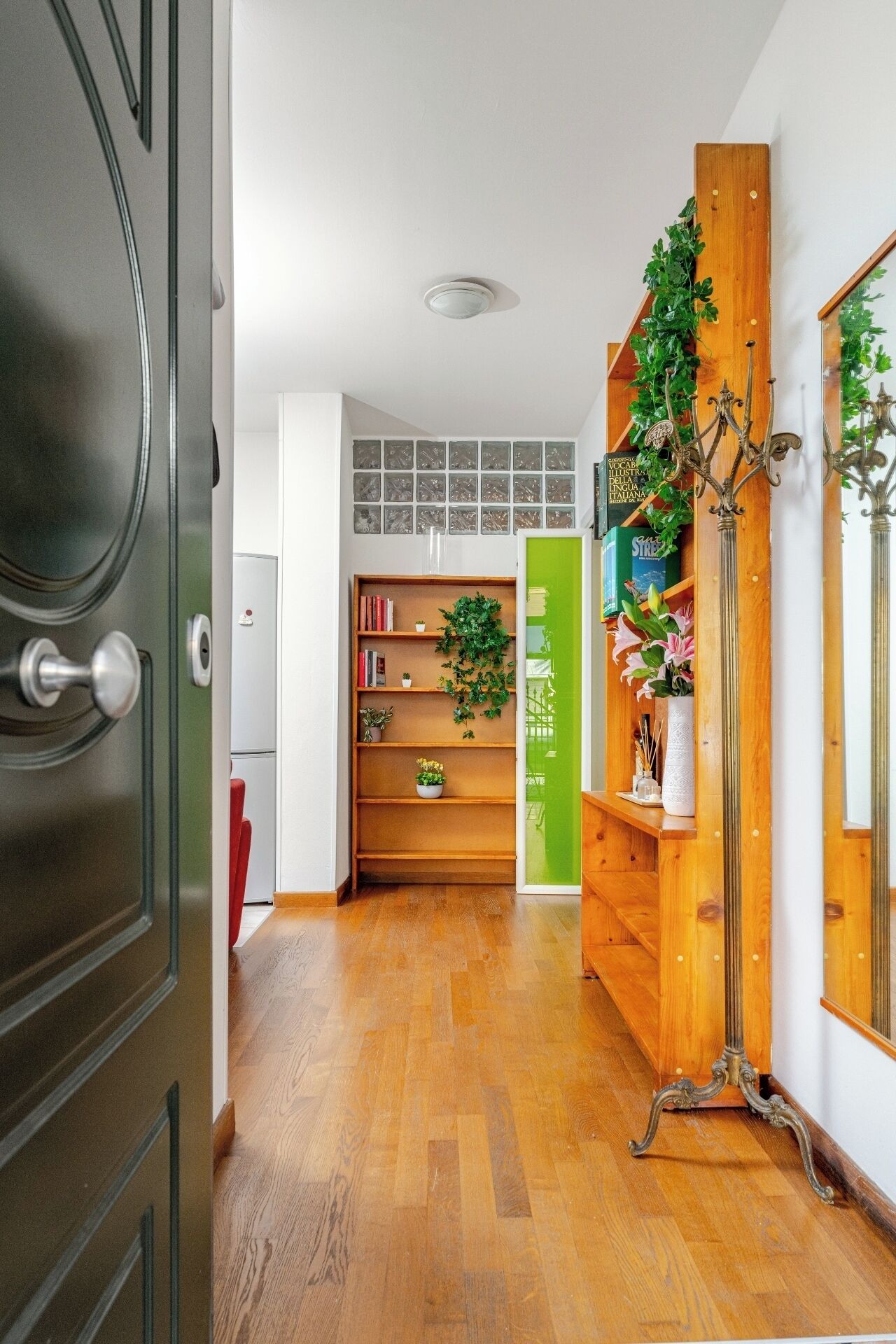 A hallway with a wooden floor, a green door, and a bookshelf with books and plants.