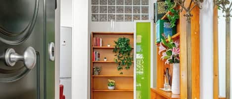 A hallway with a wooden floor, a green door, and a bookshelf with books and plants.