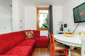 A compact living space with a red sofa, a dining table with a bowl of fruit, and a television mounted on the wall. - Venice Mestre Private Home - (Easy Access to Venice) (Venezia)