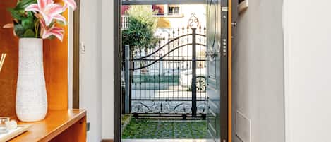 A hallway with a wooden floor, a potted plant, a metal gate, and a door leading outside.