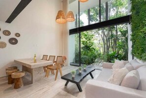 Un salon moderne doté d’une grande fenêtre, d’un coin repas avec des meubles en bois et d’une table basse noire.